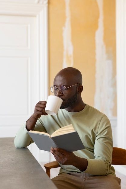Man läser en bok och dricker kaffe vid ett bord inomhus