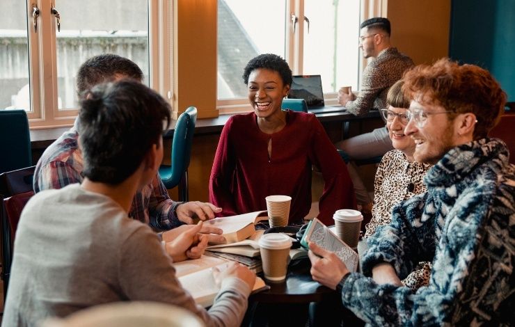 Liten grupp samtalar kring böcker och kaffe vid ett bord
