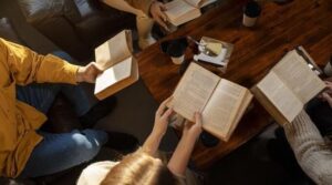 Fyra personer läser böcker runt ett träbord med kaffekoppar