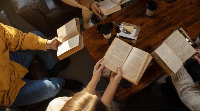 Fyra personer läser böcker runt ett träbord med kaffekoppar